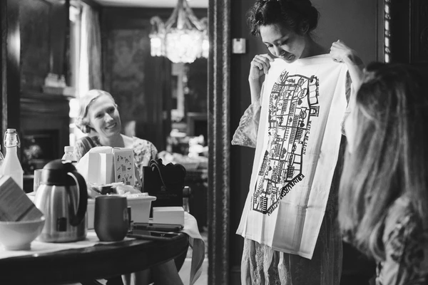 Bride smiling while showing a white t-shirt print to friends in the dressing room