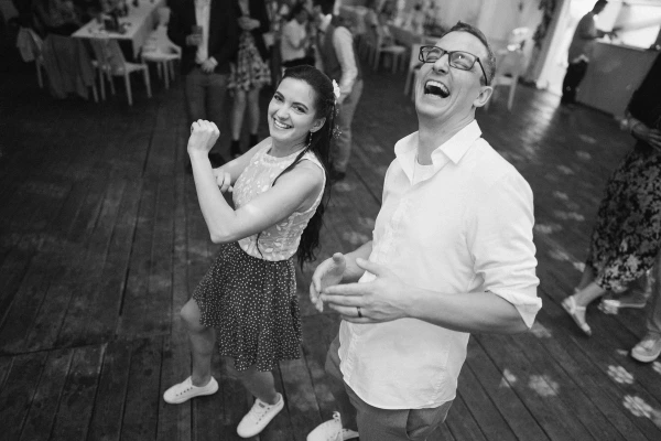 Wedding guests dancing on wooden dance floor — black and white photography, joyful celebration, casual party moment.