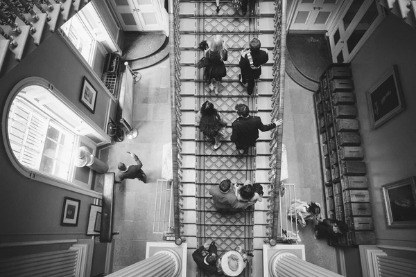 Wedding guests elegantly dressed walk up a staircase in a classical building — viewed from above