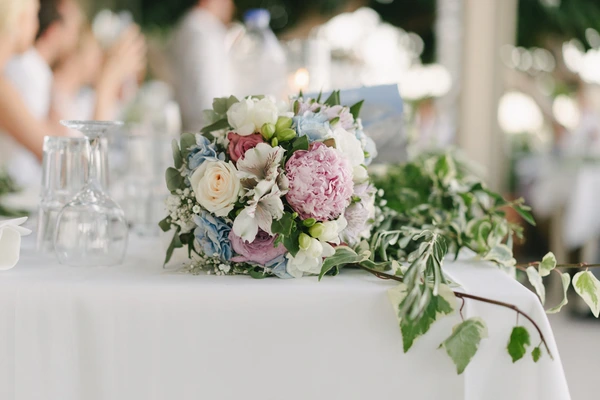 Wedding table centrepiece with pink peonies, white roses and blue hydrangea, crystal glasses