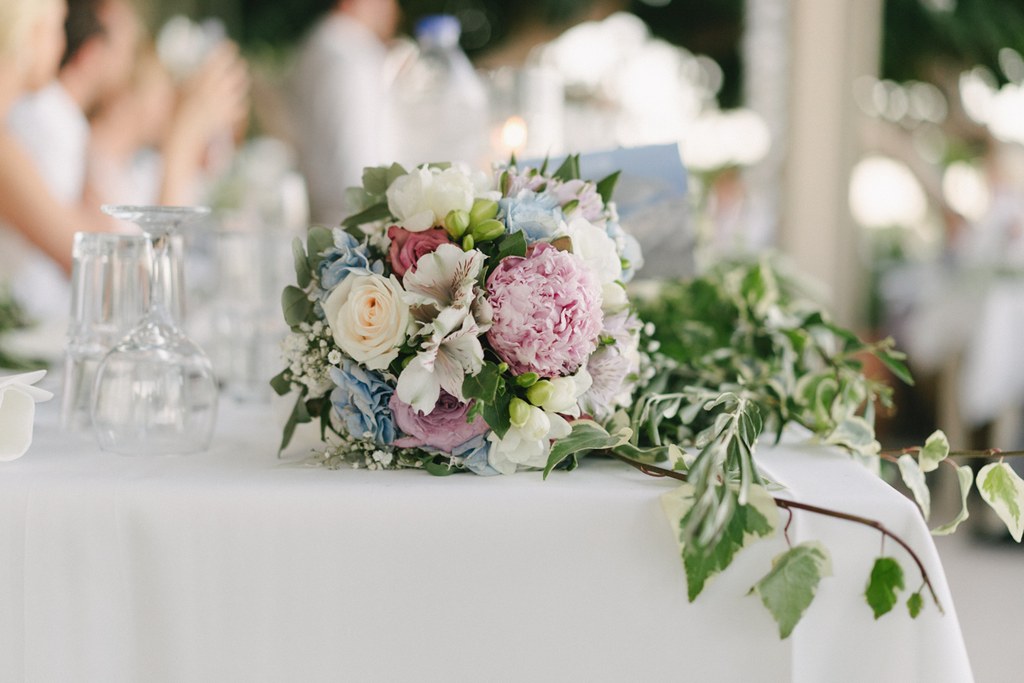 Wedding table centrepiece with pink peonies, white roses and blue hydrangea, crystal glasses