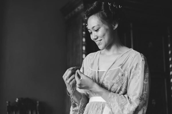 Bride gazes at her ring with a quiet smile — delicate lace dress, elegant updo, warm light