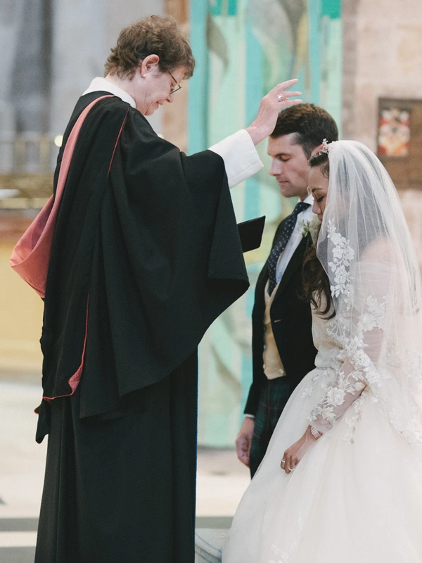 Priest gives blessing to bride and groom at the altar — bride in white lace and veil