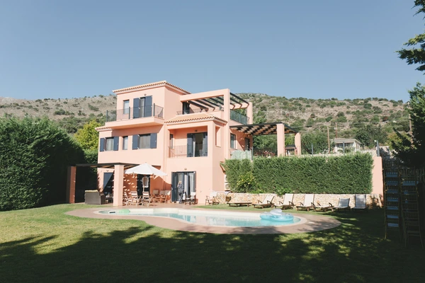 Terracotta Mediterranean villa with pool, sun loungers and a mountainous backdrop under clear sky