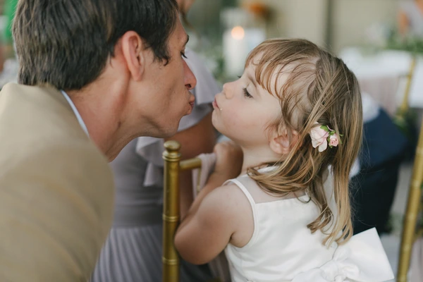 Father gives a kiss to his daughter in white dress with floral hair piece — loving wedding moment