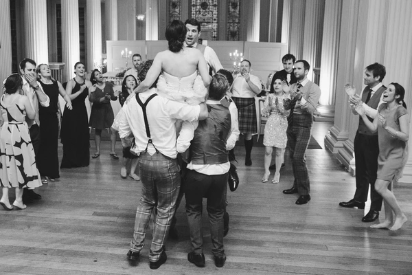 Groom lifted up among cheering guests on the dance floor — friends and family laughing