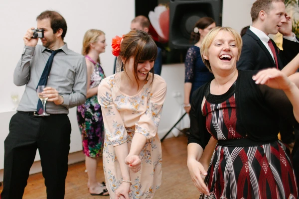 A woman dances with her arms raised on the crowded wedding dance floor, laughing joyfully. Candid documentary wedding moment.