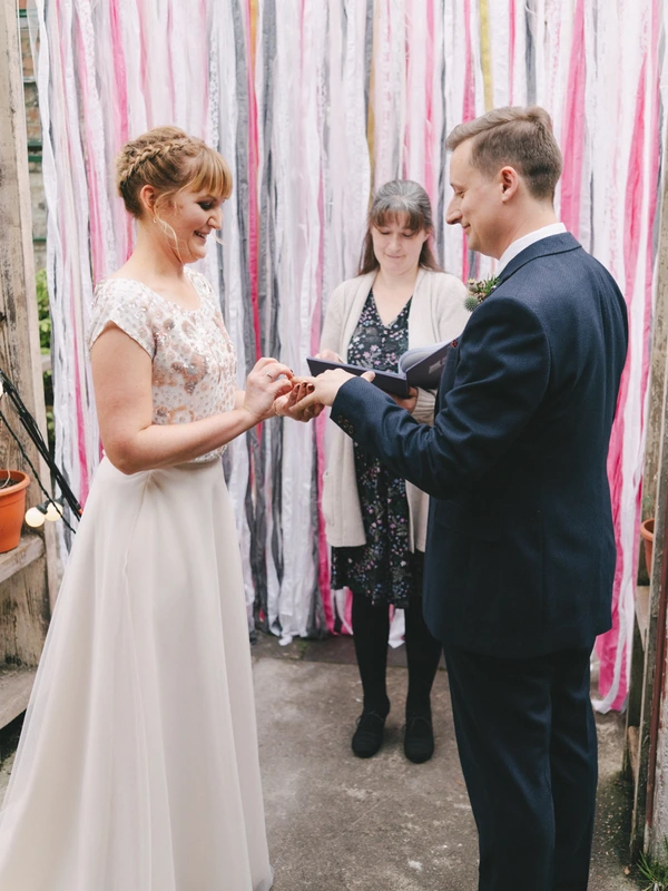 Bride and groom exchange rings at the ceremony — joyful moment against a ribbon-decorated wall