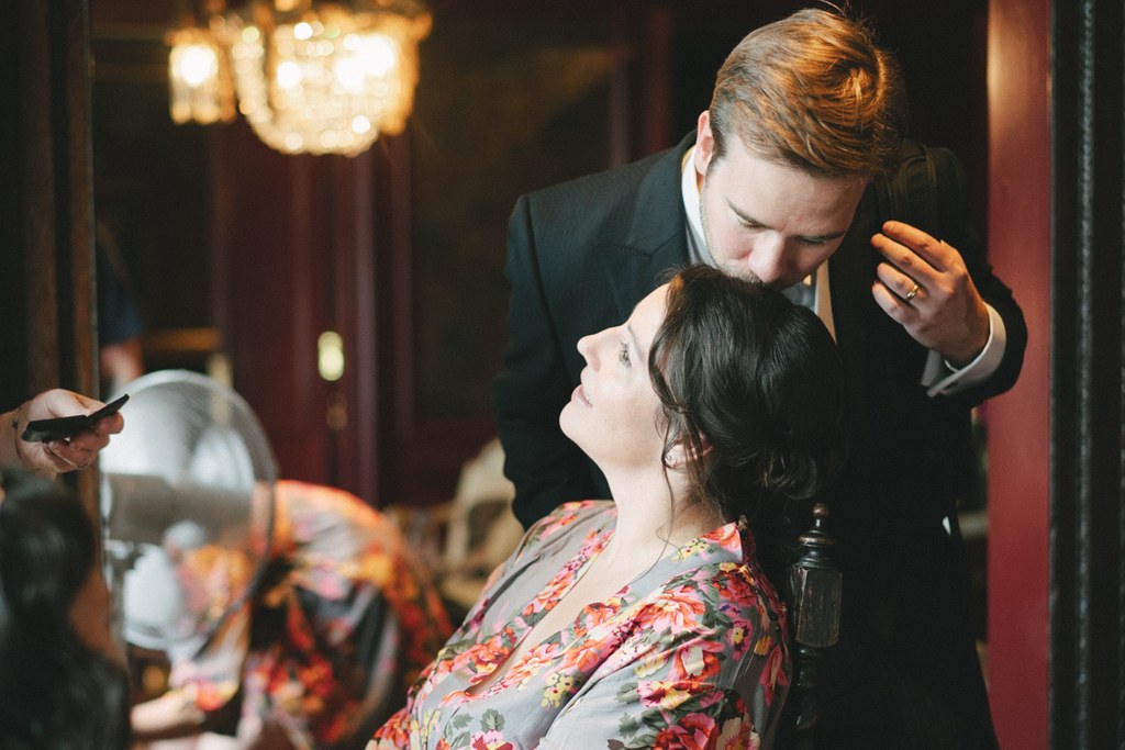 Groom with auburn hair in black suit looks lovingly at the bride in a floral robe