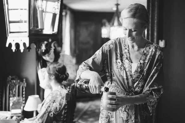 Bride in floral kimono concentrating while dressing, daylight through window, guests in background
