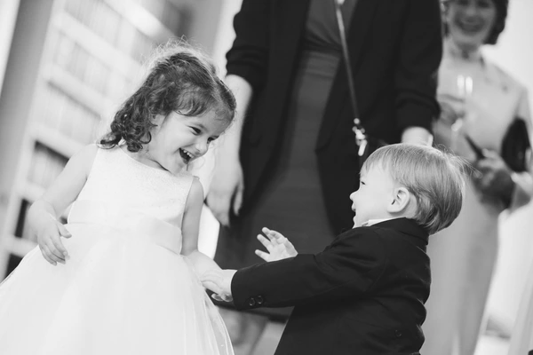 Two small children at the wedding — girl in white laughing at the boy in a black suit