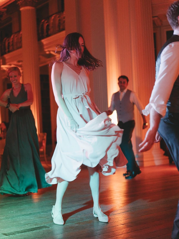 Girl in white dress dancing, gown flowing gracefully — warm gold and green light, guests watching
