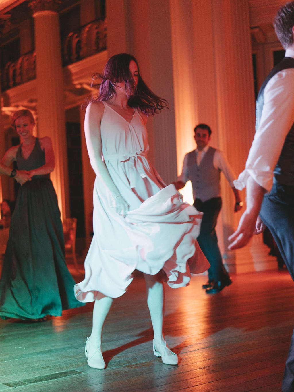 Girl in white dress dancing, gown flowing gracefully — warm gold and green light, guests watching