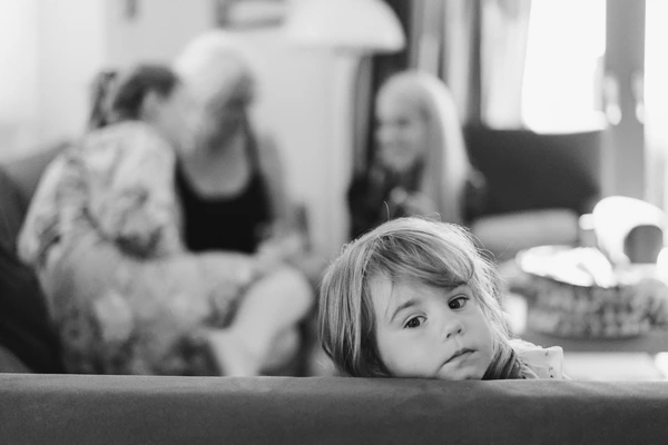 Little girl looks seriously into the camera during the wedding, adults blurred in a bright interior