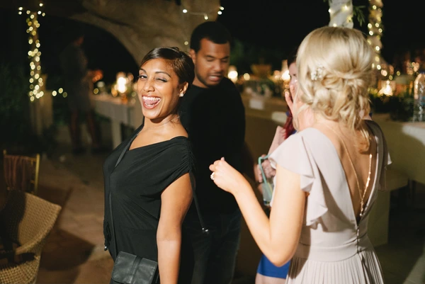 Guests enjoy the wedding reception at night — fairy lights above, smiling, cheerful mood