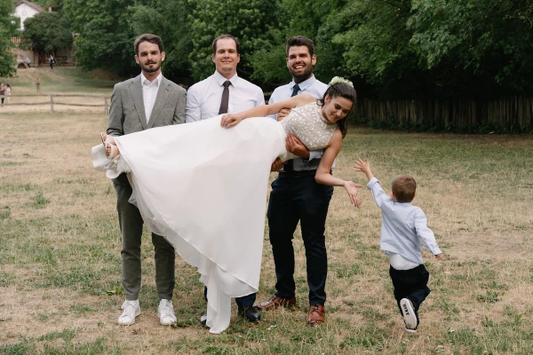 Groomsmen lifting up bride at outdoor wedding reception.