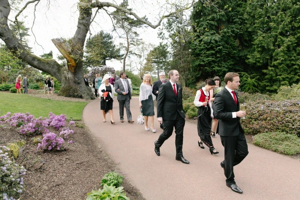 Wedding party and guests walking along a garden path through flowering borders at the Royal Botanic Garden Edinburgh after the ceremony. Candid documentary scene.