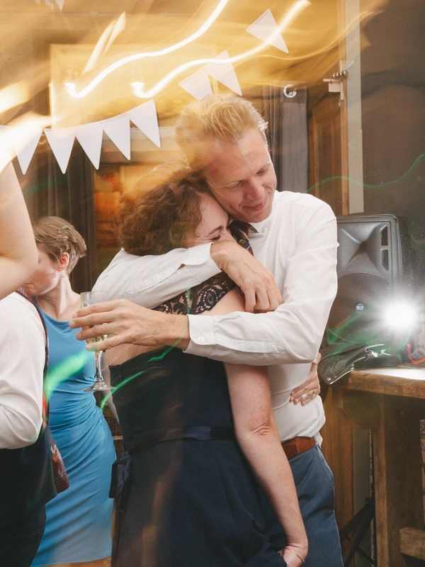 Groom in white shirt joyfully embraces the bride beside the dance floor, neon lights above