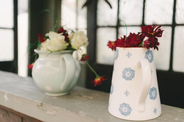 Two porcelain vases with flowers on a wooden floor, natural light through windows