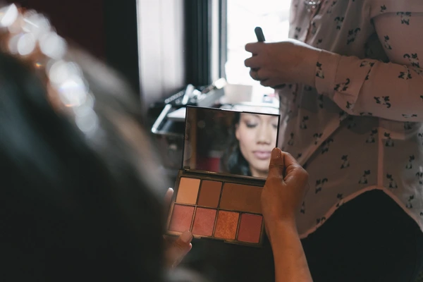 Makeup artist examines the bride's face in the mirror while holding the palette — warm light