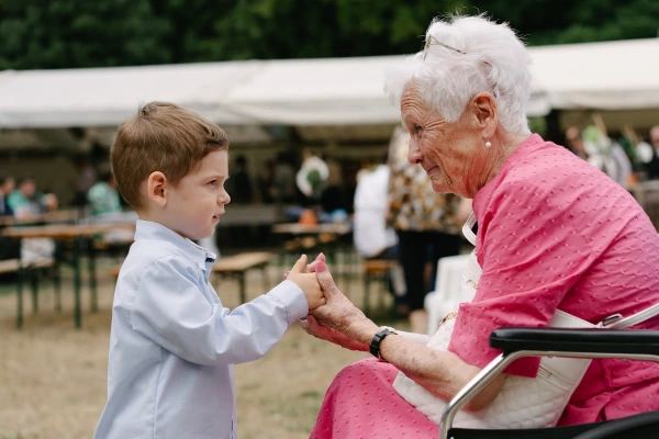 Elderly lady in a pink dress is smiling at a young boy. Wedding reception candid photo.