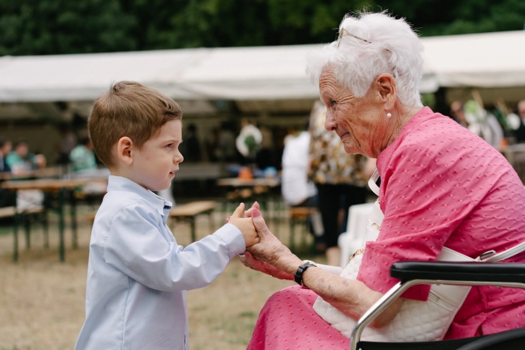 Elderly lady in a pink dress is smiling at a young boy. Wedding reception candid photo.
