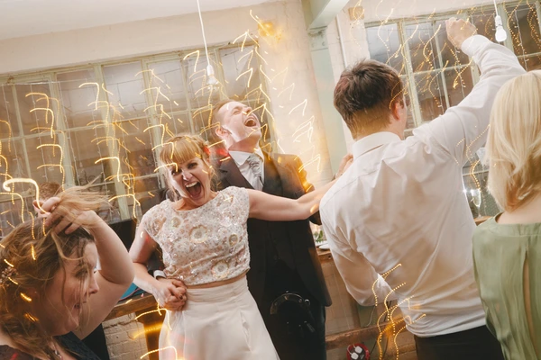 Bride in lace top dances with her husband, both laughing amid golden decorative chains