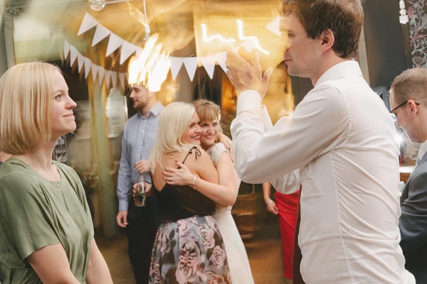 Groom in white shirt dances with a smiling guest — golden decoration, warmly lit room