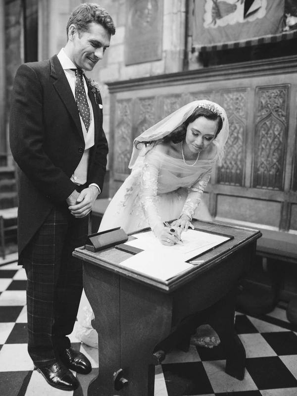 Groom smiling as he watches the bride sign the marriage document during the church ceremony