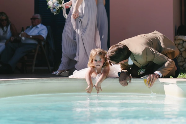 Groom helps a little girl into the pool — joyful moment, bride watching, guests looking on