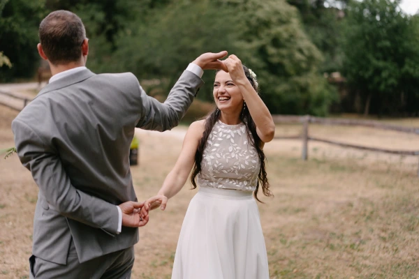 Couple spinning and dancing together with joyful expression at outdoor wedding under natural sky.