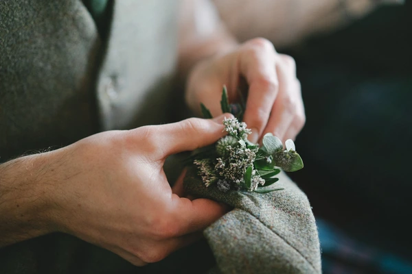 Bride and groom's hands beside the green and white bouquet — warm natural light, intimate moment