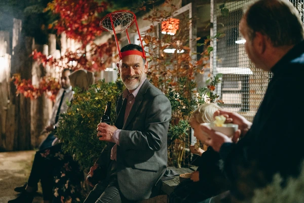 Man with a basketball bandana laughs at the dark wedding party — greying beard, grey suit