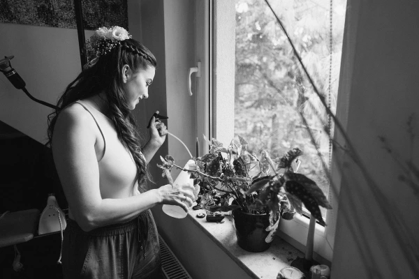 Black and white photo of the bride watering plants by the window on her wedding morning.