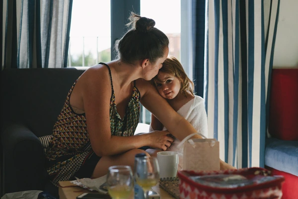 Mother kisses her daughter at the dining table — warm light, warmth and love radiate from the moment