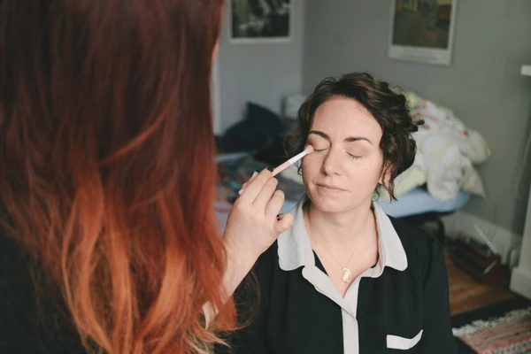 Makeup artist applies eyeshadow with a white brush on the bride in quiet room lighting