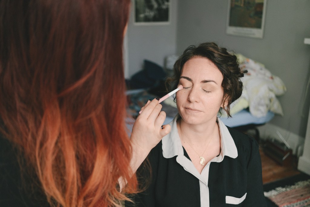 Makeup artist applies eyeshadow with a white brush on the bride in quiet room lighting