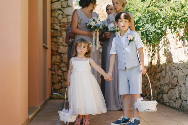 Two children walk hand in hand scattering white flowers — girl in white dress, boy in light suit