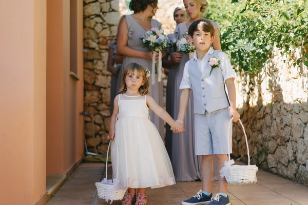 Two children walk hand in hand scattering white flowers — girl in white dress, boy in light suit