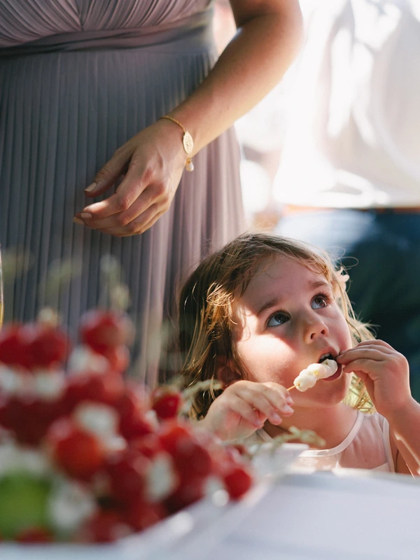 Little girl in pink eats something sweet at the wedding dinner, woman's gold bracelet above her