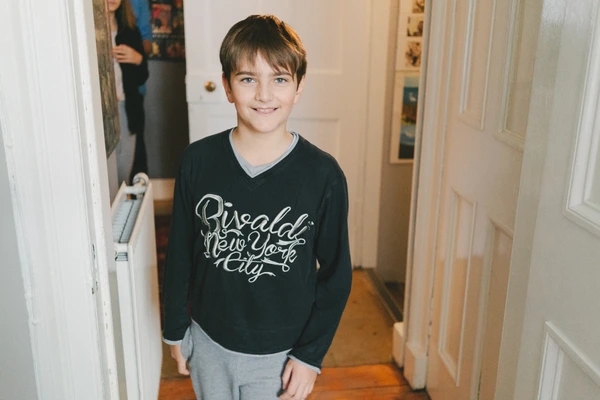 Boy smiling in a black New York sweatshirt in a hallway, warm natural light