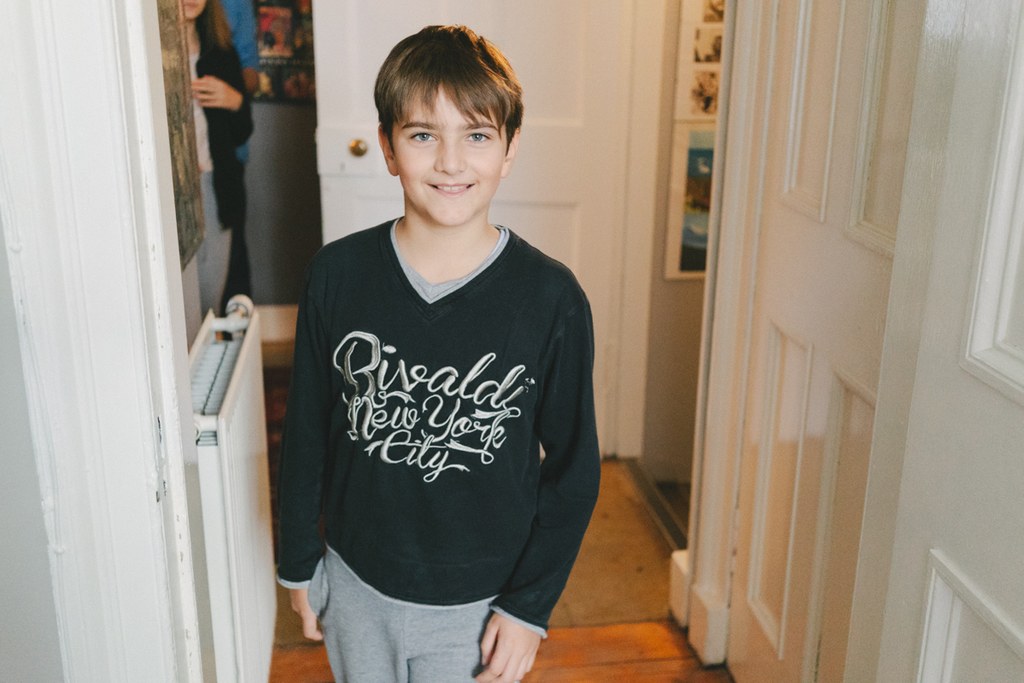 Boy smiling in a black New York sweatshirt in a hallway, warm natural light