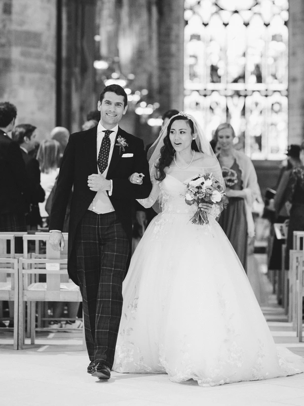 Bride and groom walk down the aisle after the ceremony — white lace and veil, blurred guests behind
