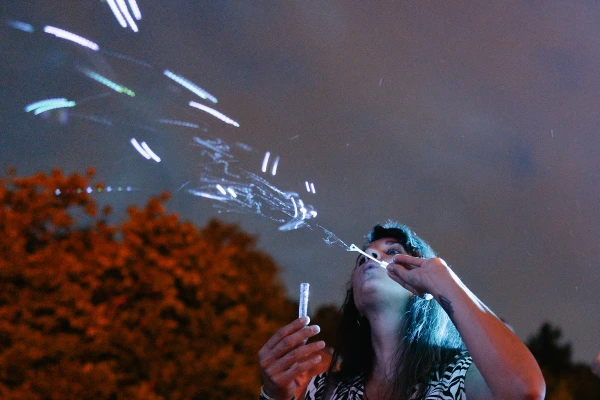 Female guest blowing sparkler bubbles at night — long exposure, magical light trails, celebratory wedding moment outdoors.