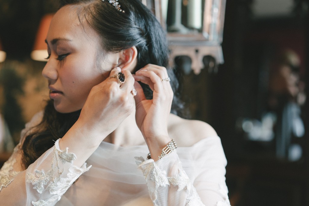 Bride in white lace carefully puts on an earring — jewels on her hand, focused expression