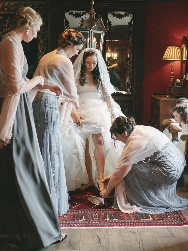 Final preparations — helpers arrange the bridal veil and lace skirt, bride waits peacefully