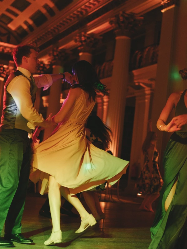 Young couple dances — bride's yellow dress lifts as groom holds her. Warm orange and green light.