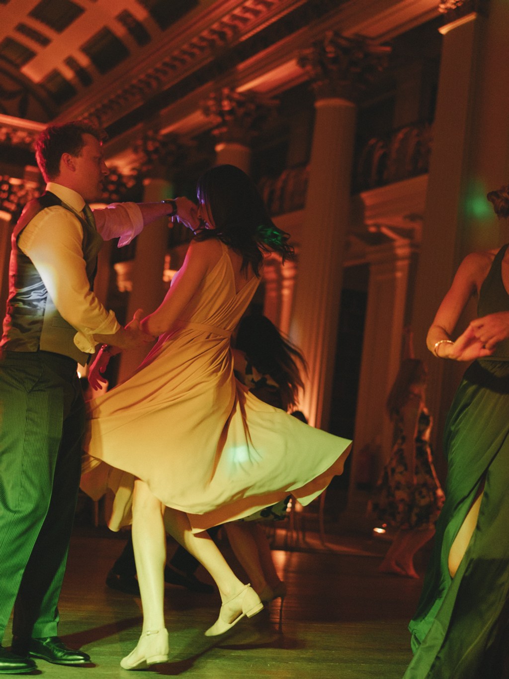 Young couple dances — bride's yellow dress lifts as groom holds her. Warm orange and green light.