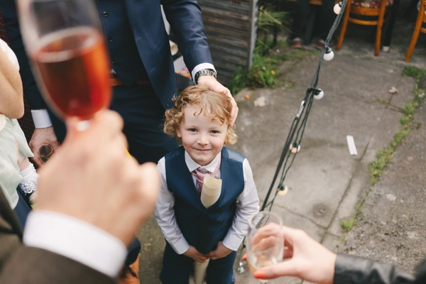 Little girl with curly hair smiles, adults celebrating with champagne glasses in the garden