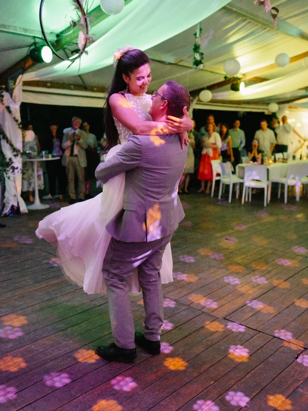 Bride and groom dancing joyfully at evening wedding reception with dramatic colored lighting.